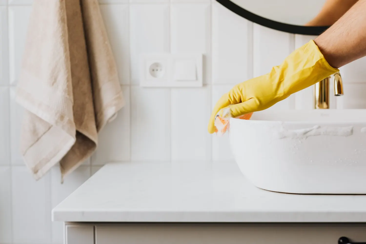 Stock photo of a gloved hand cleaning a bathroom sink faucet