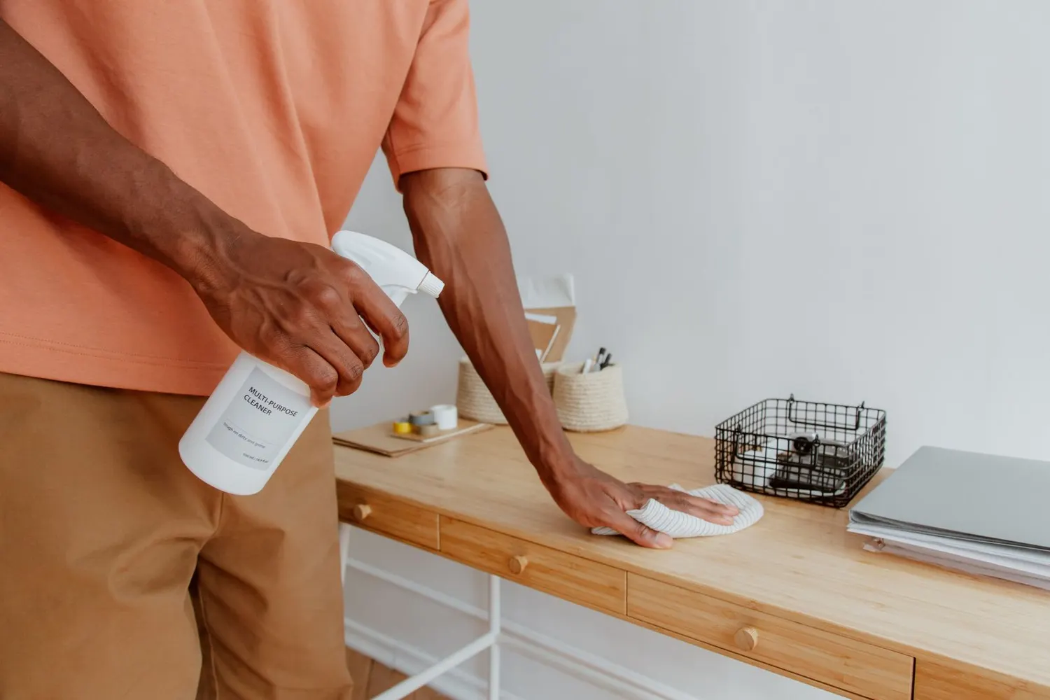 Stock photo of a man spraying and wiping a wooden desk